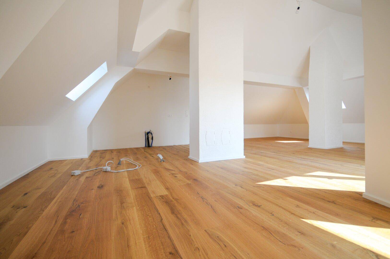 Offener Dachgeschossbereich mit Holzboden und schrägen Wänden, durchflutet von natürlichem Licht.