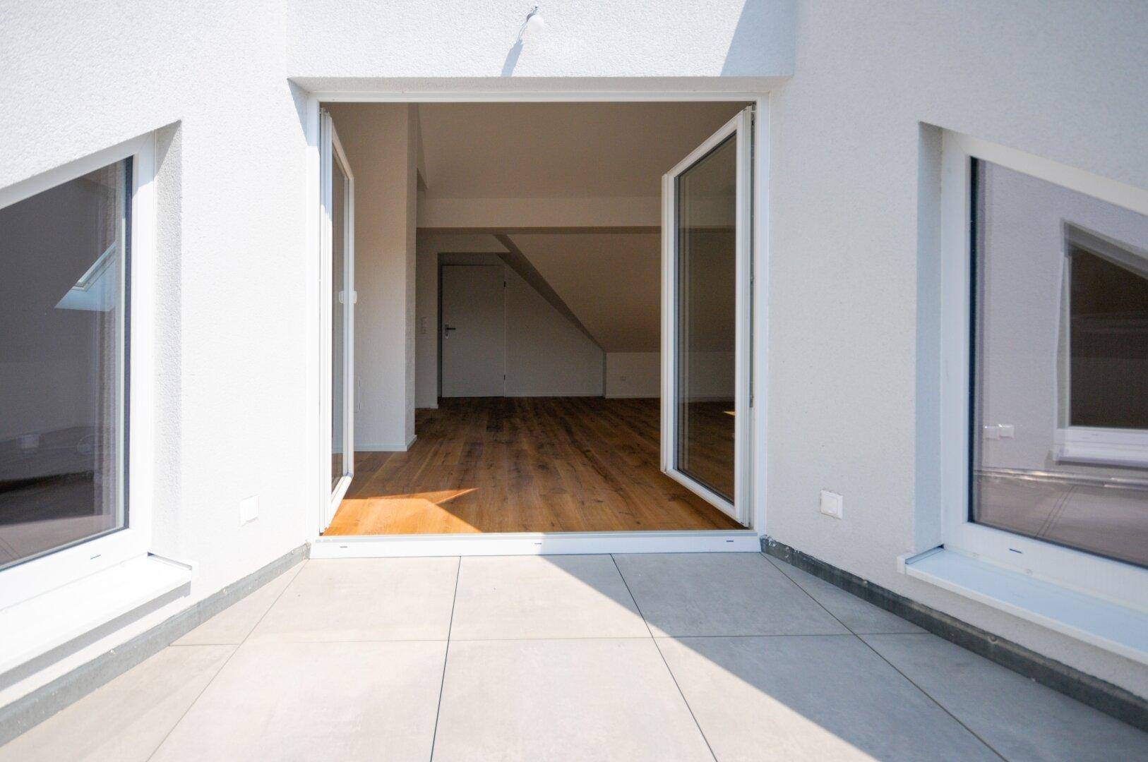 Sonniger Terrassenbereich mit Fliesenboden und Zugang zu einem hellen Innenraum im Dachgeschoss.
