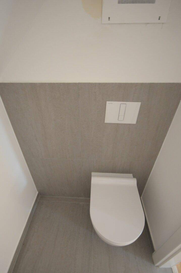 Separates WC mit Wand-WC und grauen Fliesen, praktisch und platzsparend gestaltet.