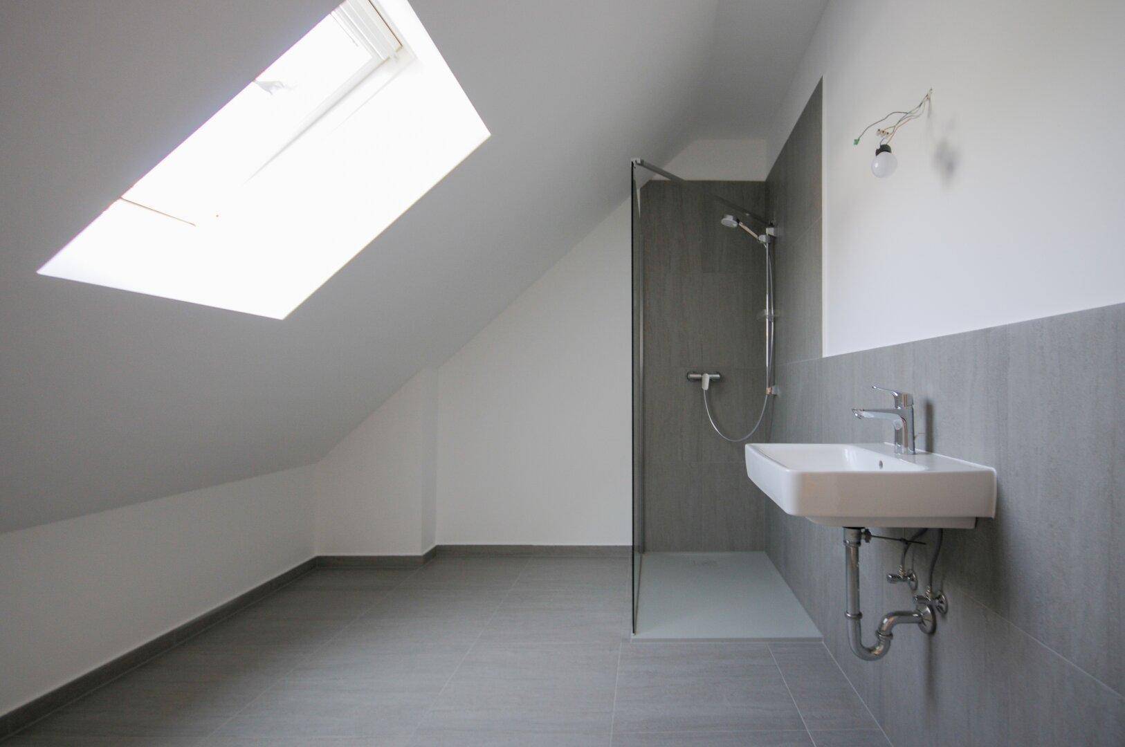 Modernes Badezimmer im Dachgeschoss mit Dusche, Waschbecken und Dachfenster für natürliches Licht.