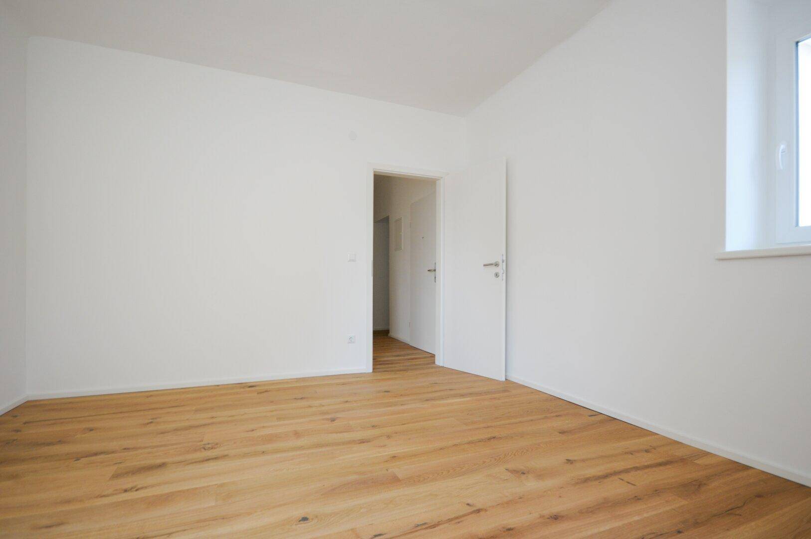 Leeres Schlafzimmer mit hellem Holzboden und einem Fenster für natürliches Licht.