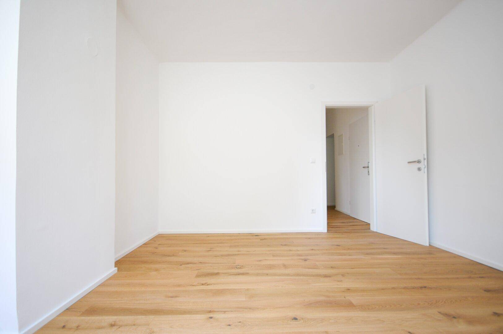 Leerer Raum mit hellen Wänden und neuem Holzboden, bereit für die Einrichtung.