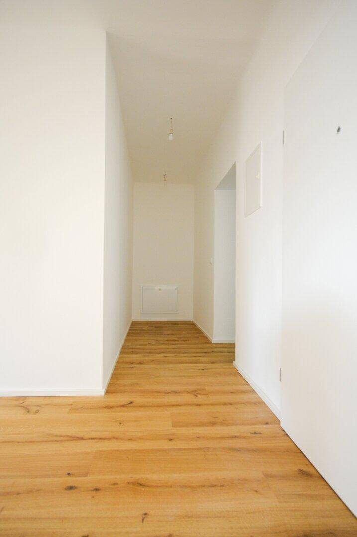 Langer, heller Flur mit Holzboden und weißen Wänden, der zu weiteren Räumen führt.