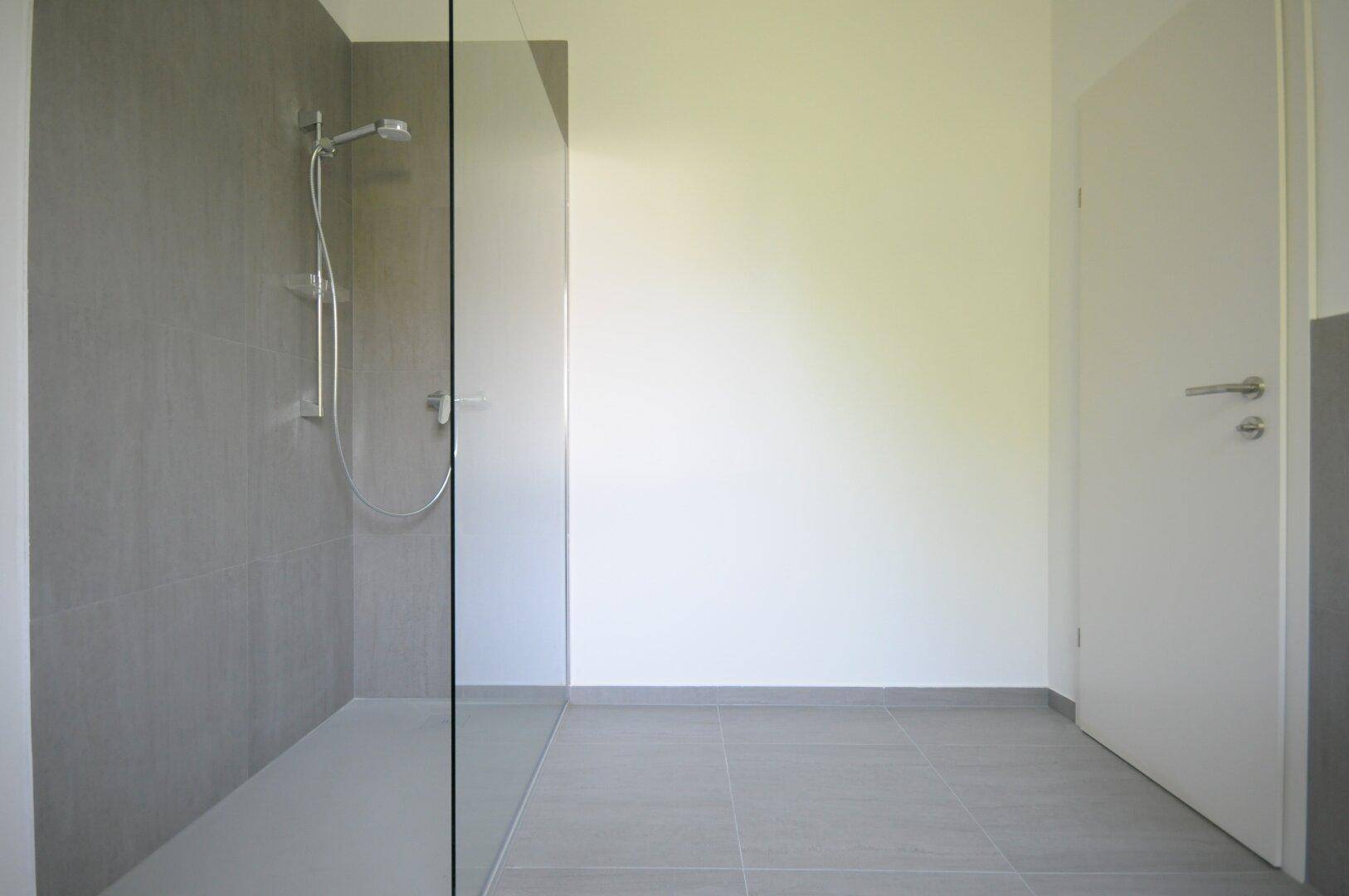 Modernes Badezimmer mit grauen Fliesen und einer begehbaren Dusche.