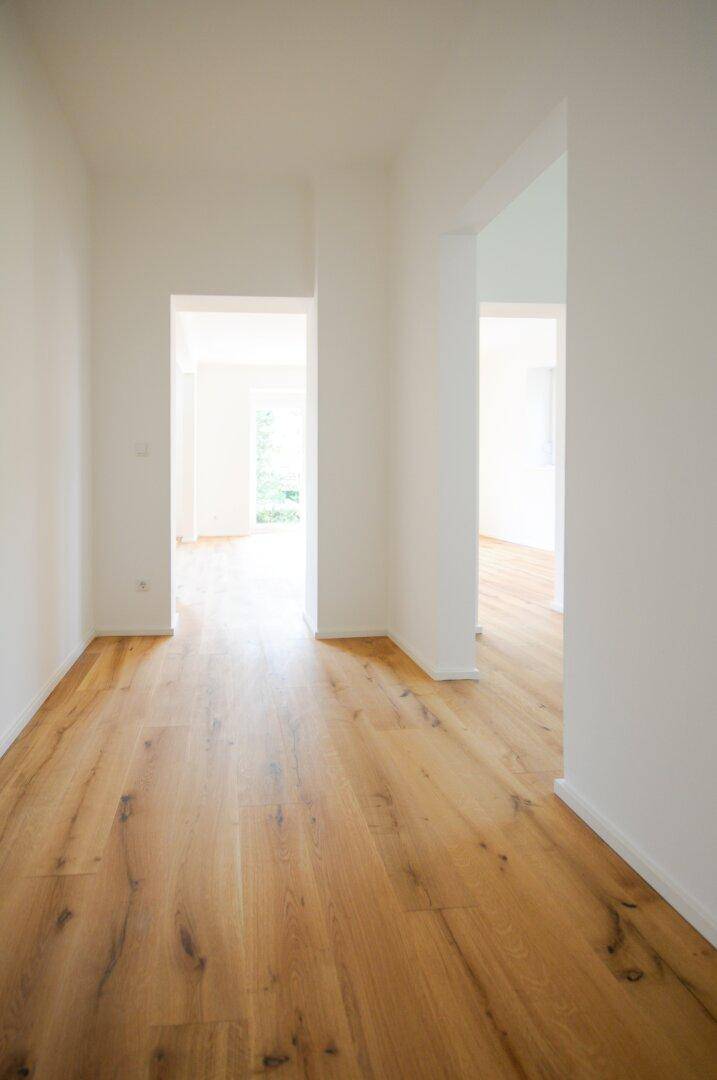 Geräumiger Wohnbereich mit hellem Holzboden und offenen Durchgängen.