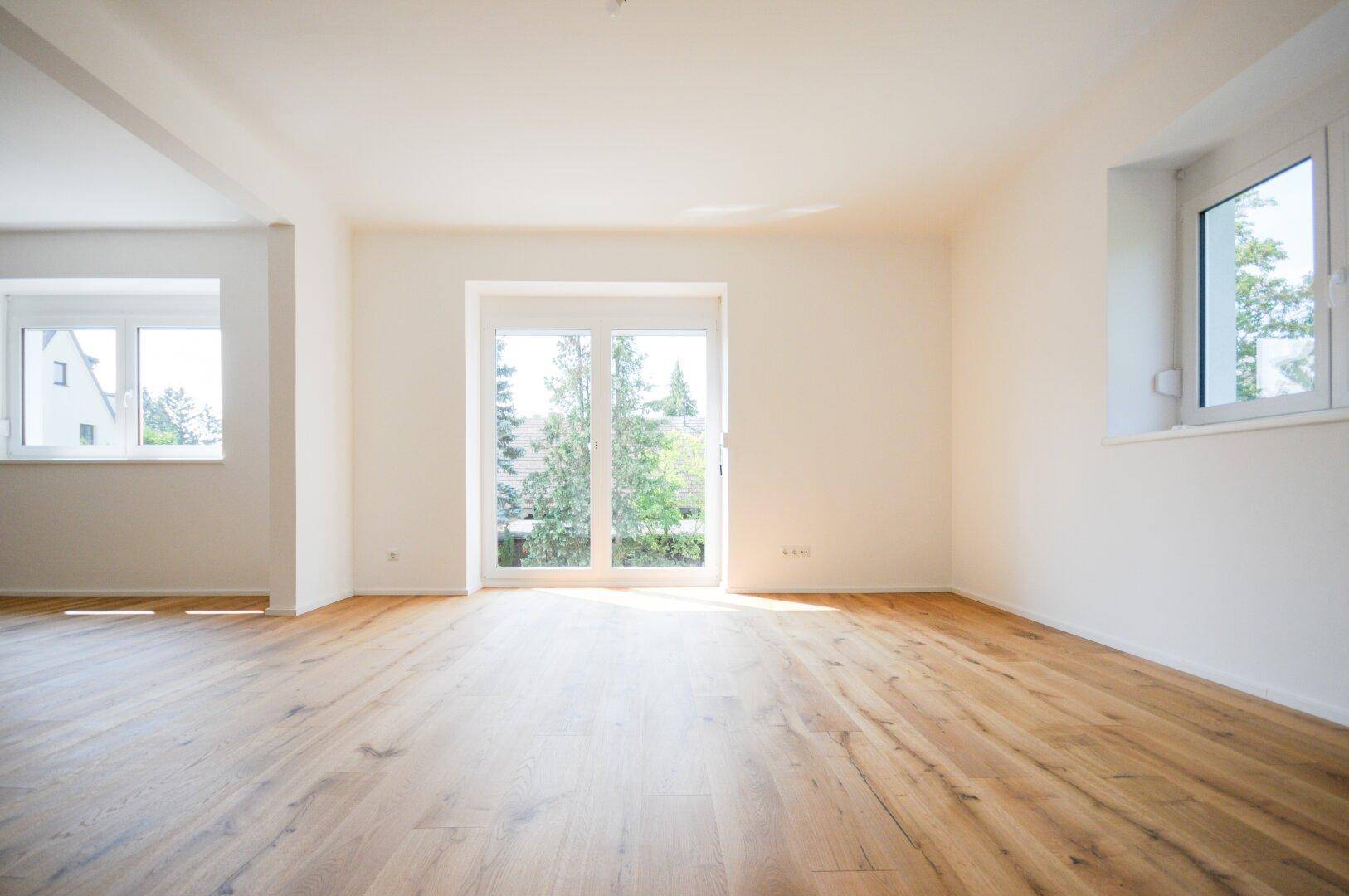 Heller Wohnraum mit Holzboden, großen Fenstern und Zugang zum Außenbereich.