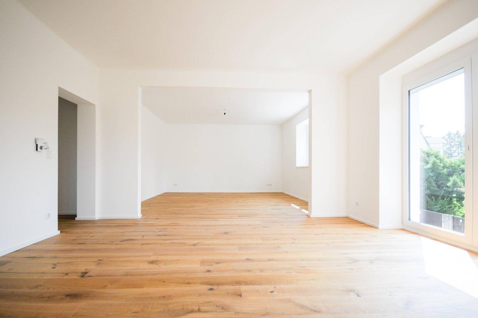 Lichtdurchflutetes Wohnzimmer mit Holzboden und Zugang zu einem Außenbereich durch eine große Tür.