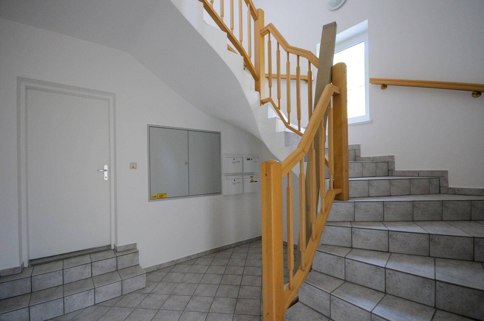 Treppenhaus mit Holzgeländer und gefliesten Stufen, das zu den oberen Etagen führt.