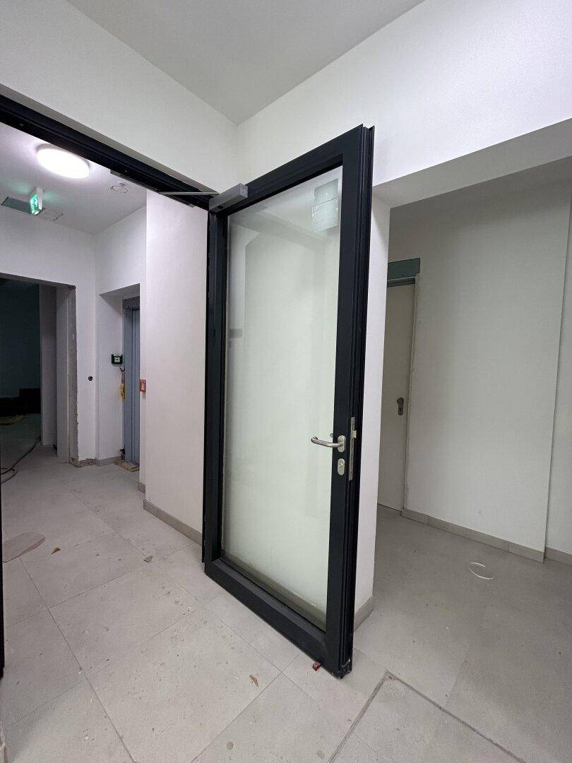 Eingangsbereich oder Flur im Rohbauzustand mit großer Glastür und Aufzug im Hintergrund.