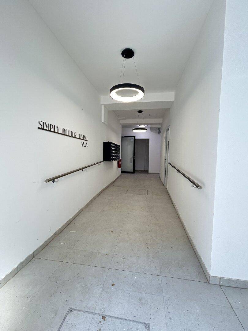 Langer, heller Flur mit modernen Deckenleuchten, Handläufen und Briefkästen an der Wand.