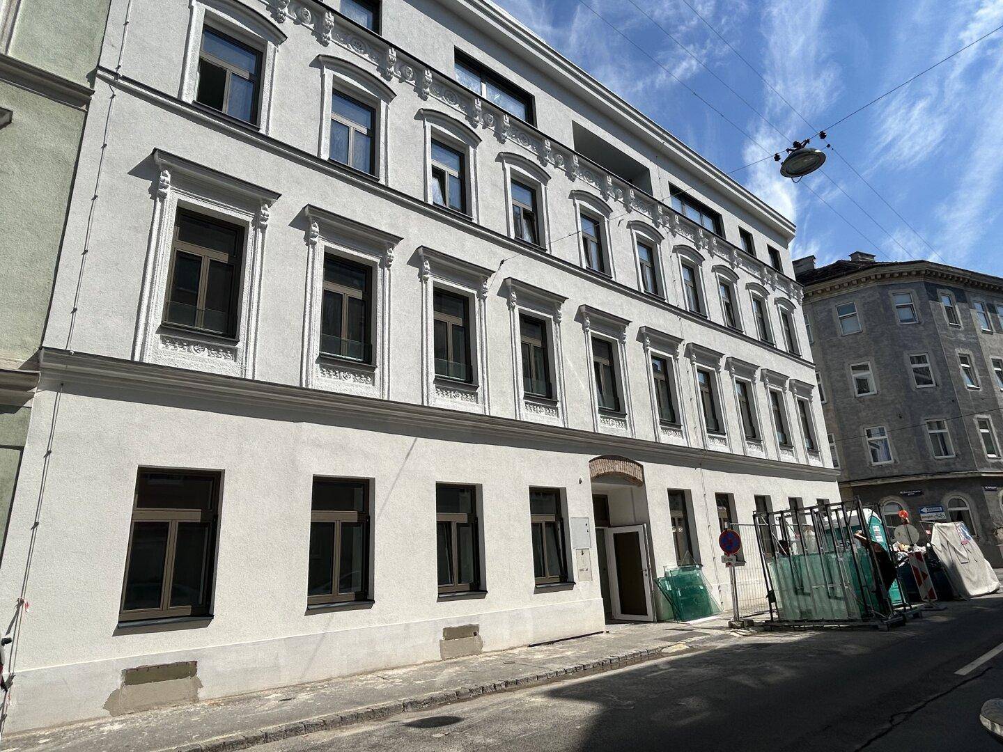 Außenansicht eines renovierten Mehrfamilienhauses mit weißer Fassade und vielen Fenstern.