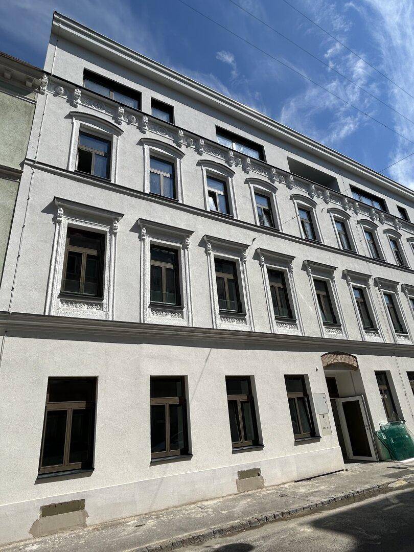 Fassade eines renovierten Mehrfamilienhauses mit vielen Fenstern und klassischer Architektur unter blauem Himmel.