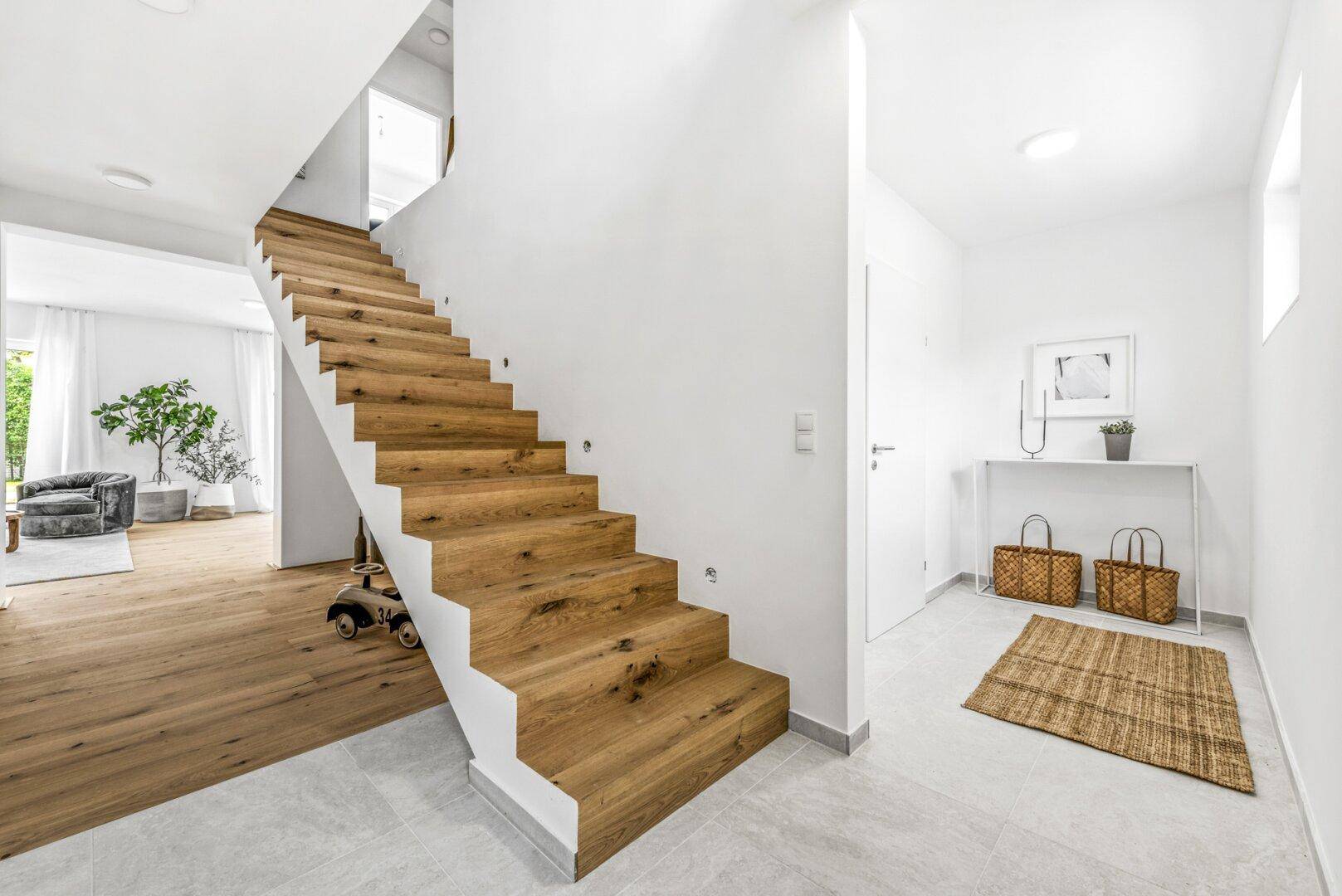 Heller Eingangsbereich mit Holztreppe und Fliesenboden, der zu den oberen Etagen führt.