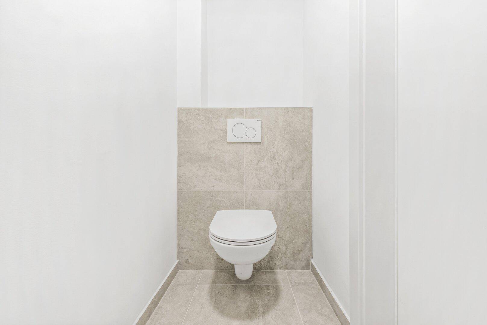Modernes Gäste-WC mit wandhängender Toilette und hellen Fliesen.