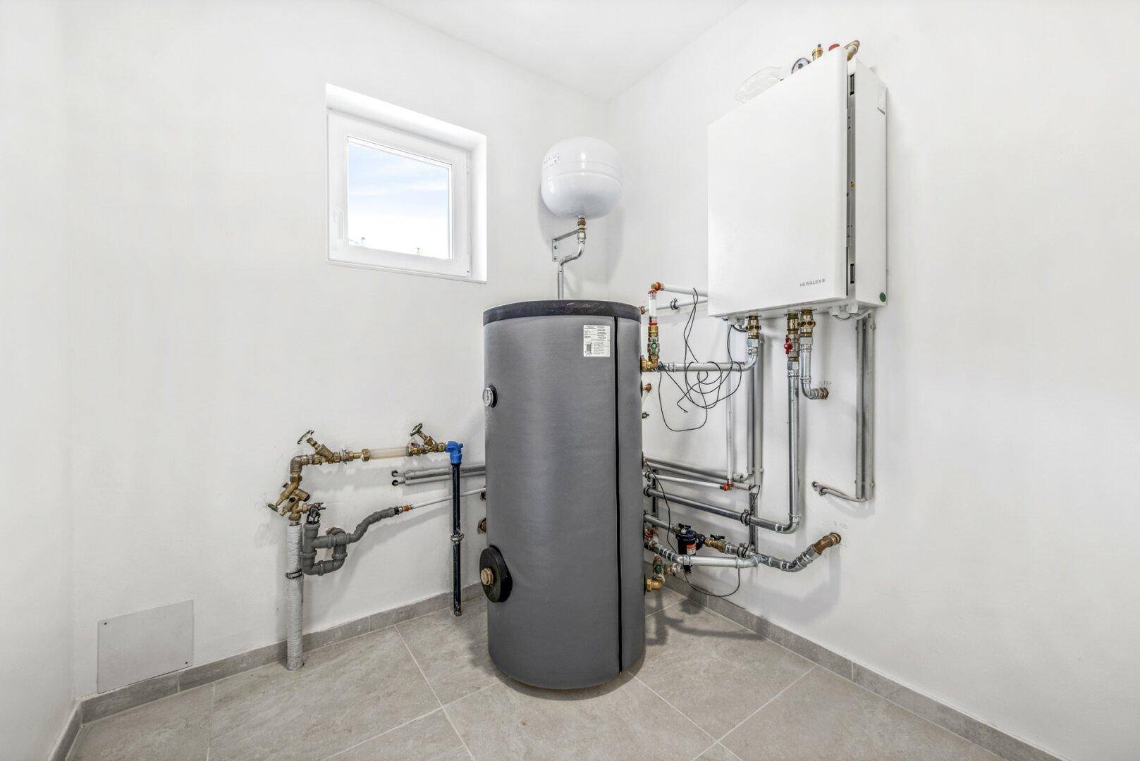 Technikraum mit Heizungsanlage, Warmwasserspeicher und kleinem Fenster.