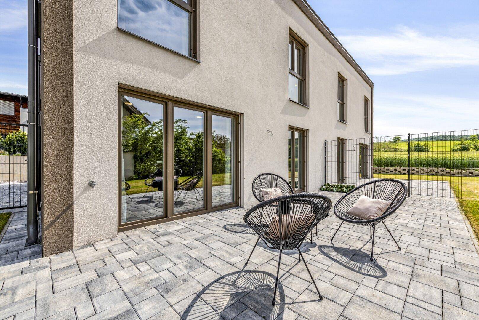 Sonniger Terrassenbereich mit modernen Gartenmöbeln und Zugang zum Garten.