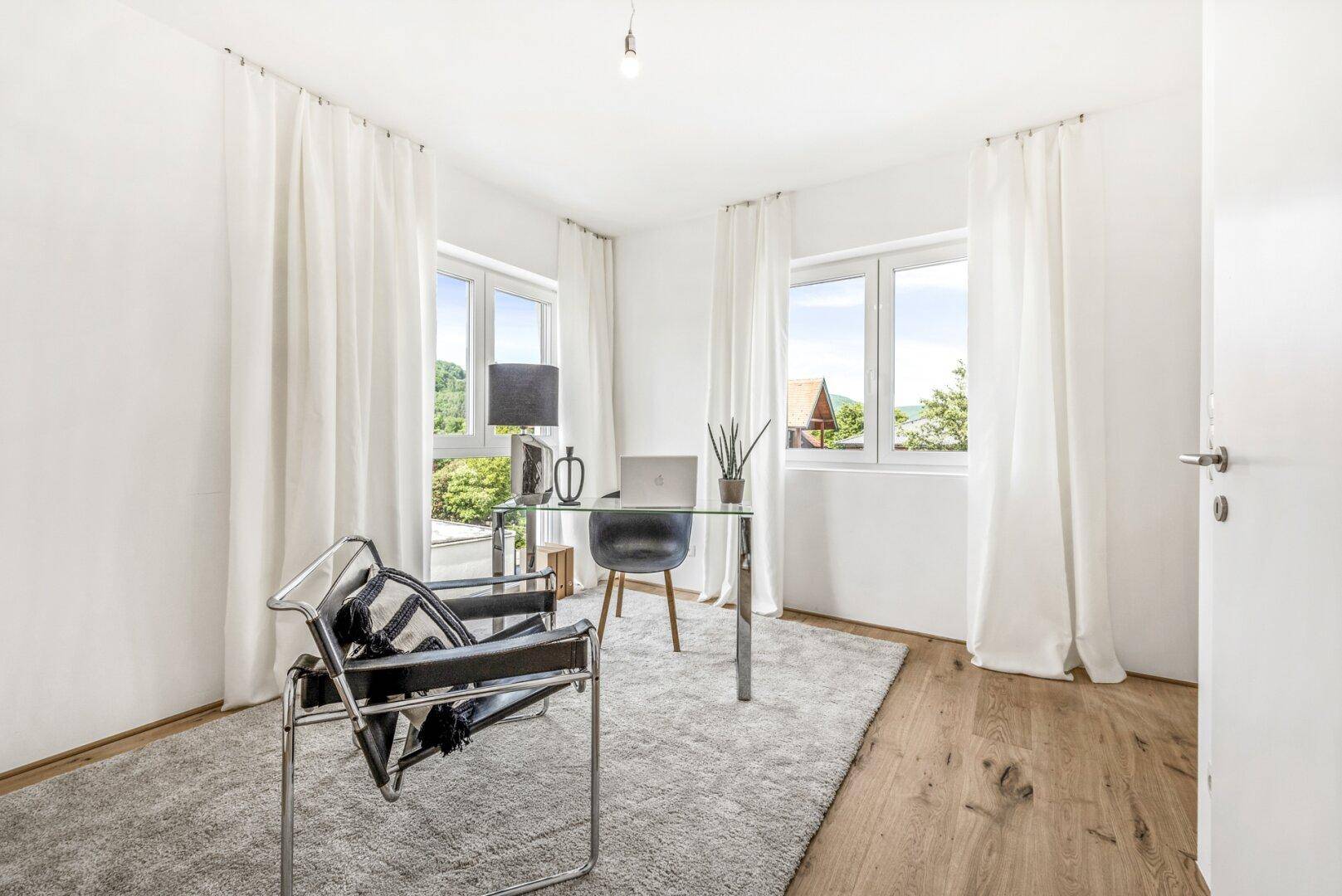 Helles Arbeitszimmer mit Holzboden, großem Fenster und modernem Schreibtisch.