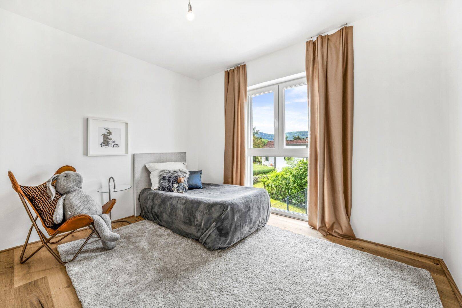 Gemütliches Schlafzimmer mit Holzboden, großem Fenster und Blick ins Grüne.
