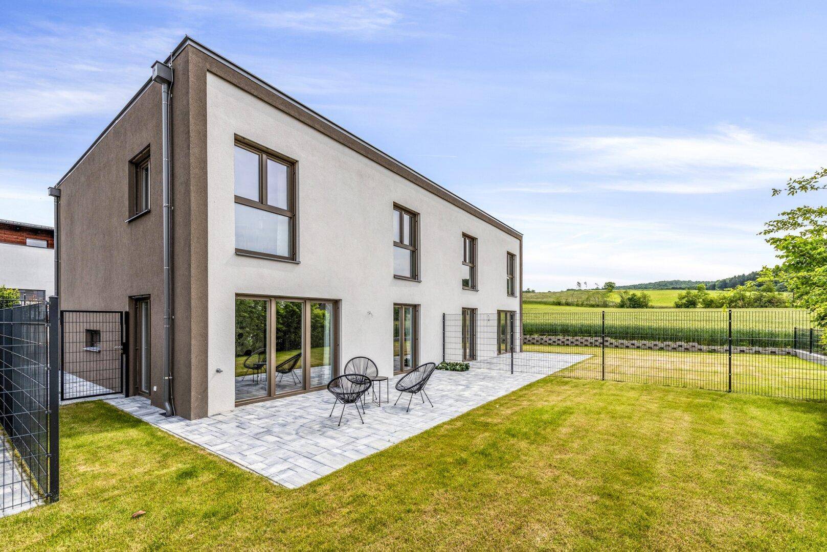 Sonniger Außenbereich mit Terrasse, Gartenmöbeln und Blick auf die grüne Landschaft.