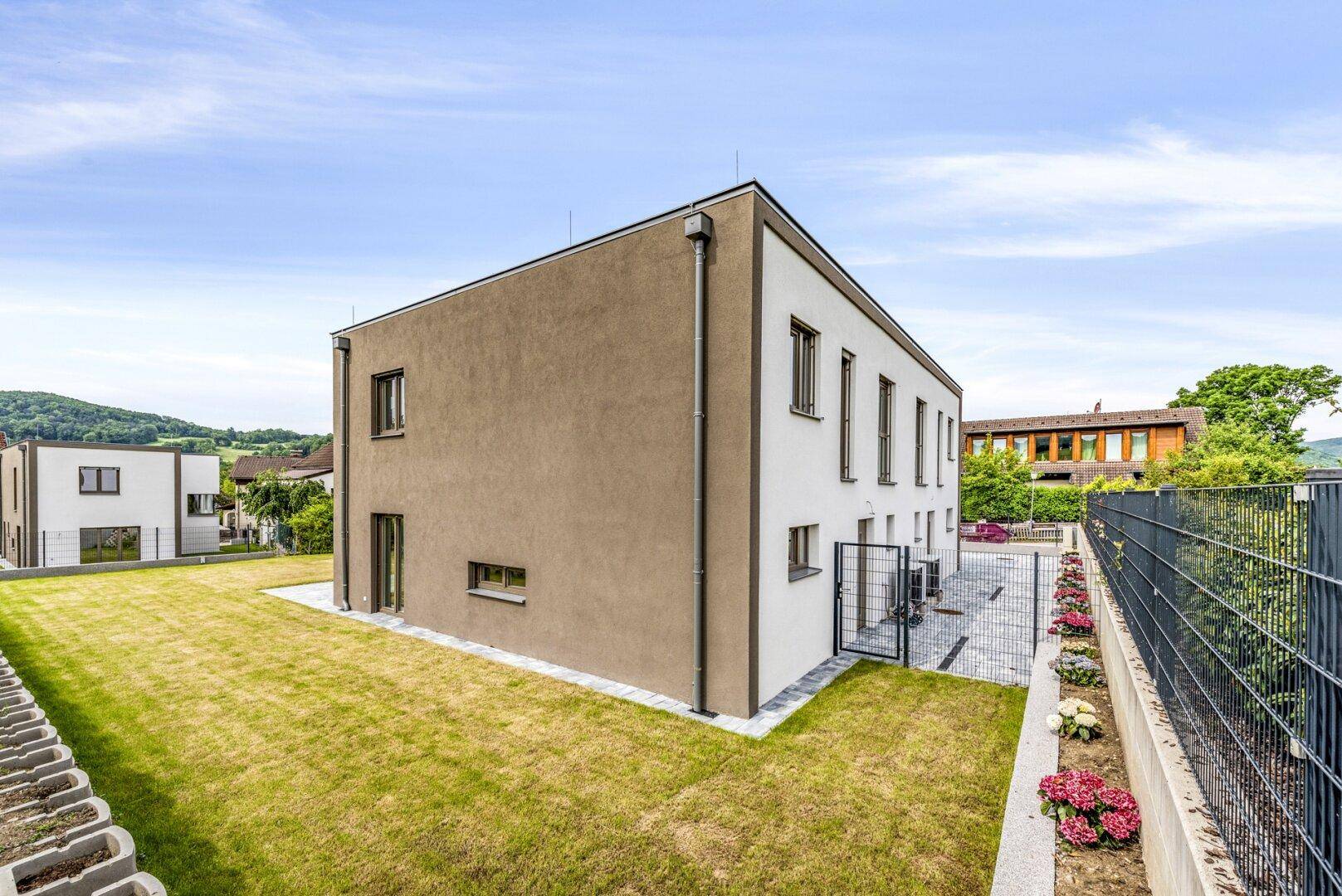 Modernes Reihenhaus mit brauner und weißer Fassade und gepflegtem Rasen.
