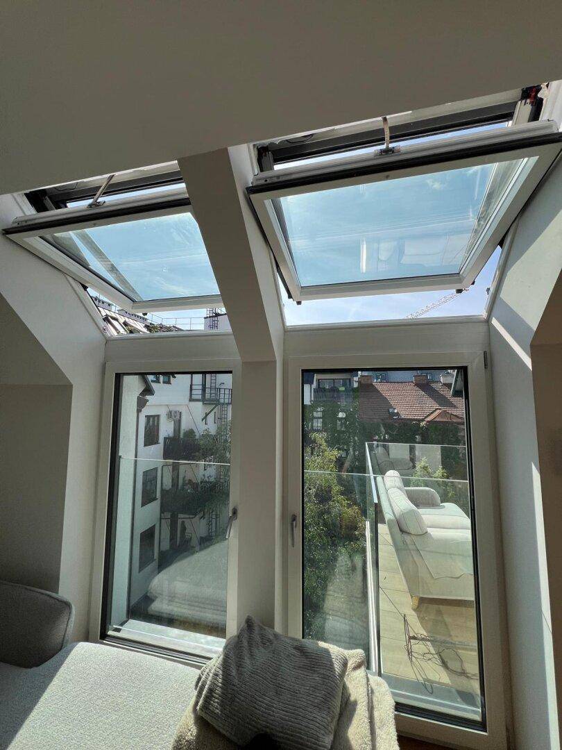 Heller Wohnbereich mit großen Dachfenstern und Zugang zu einer Terrasse mit Glasgeländer.