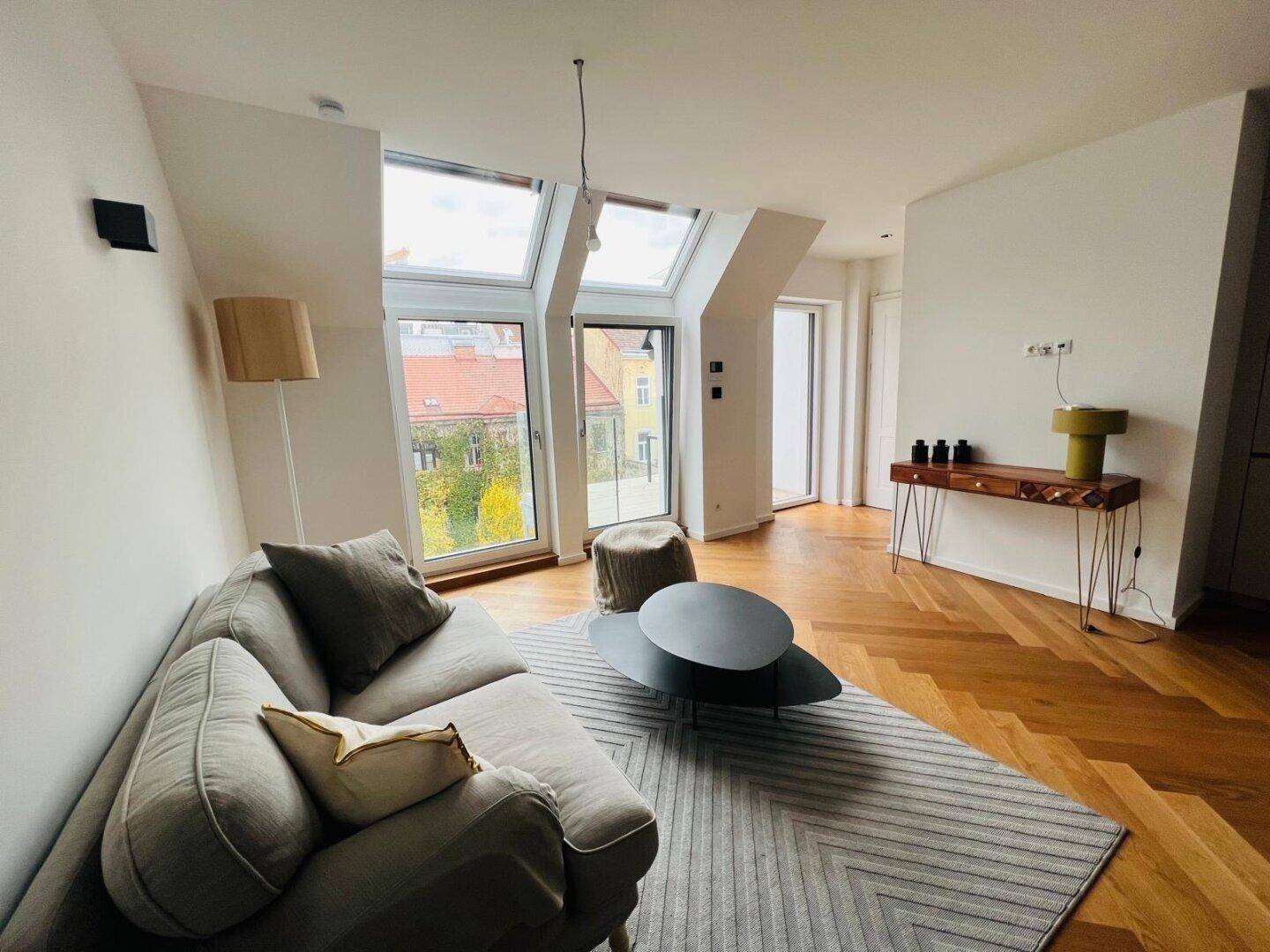 Gemütliches Wohnzimmer mit Parkettboden, großen Fenstern und Blick ins Grüne.