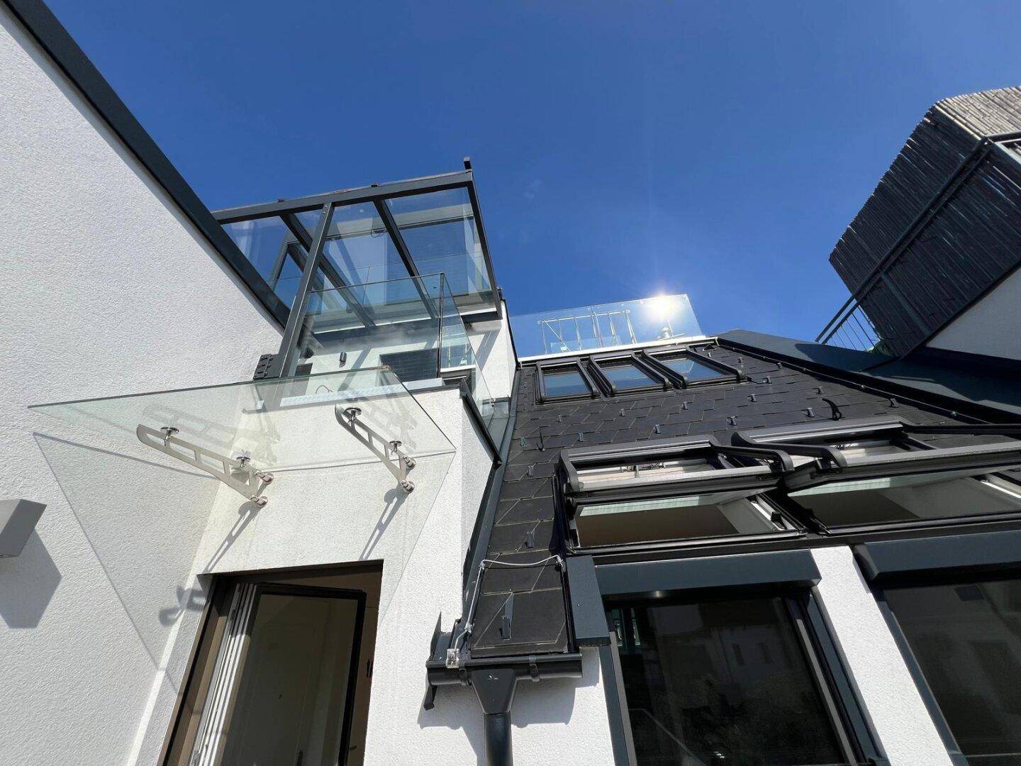 Moderne Architektur mit Glasüberdachung und Dachfenstern unter blauem Himmel.