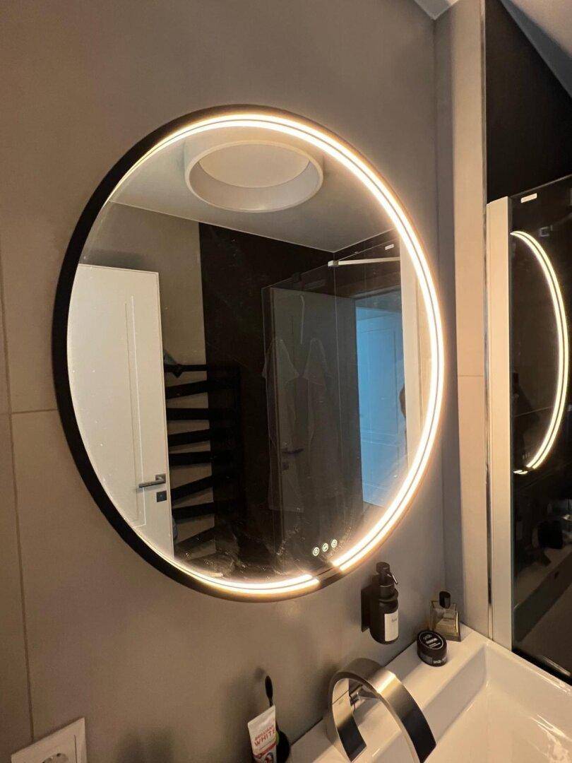 Modernes Badezimmer mit beleuchtetem Rundspiegel und minimalistischen Armaturen.