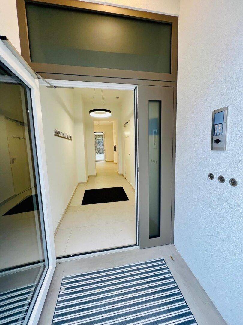Moderner Eingangsbereich mit offener Tür, die in einen hellen Flur führt.