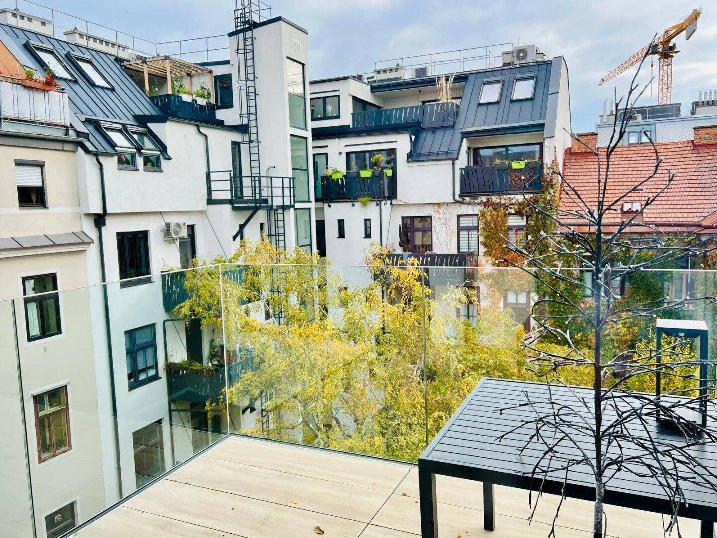 Dachterrasse mit Glasgeländer und Blick auf die umliegenden Gebäude und Bäume.