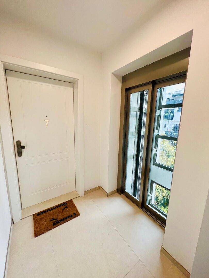 Heller Flur mit moderner Tür und Blick durch große Fenster ins Freie.