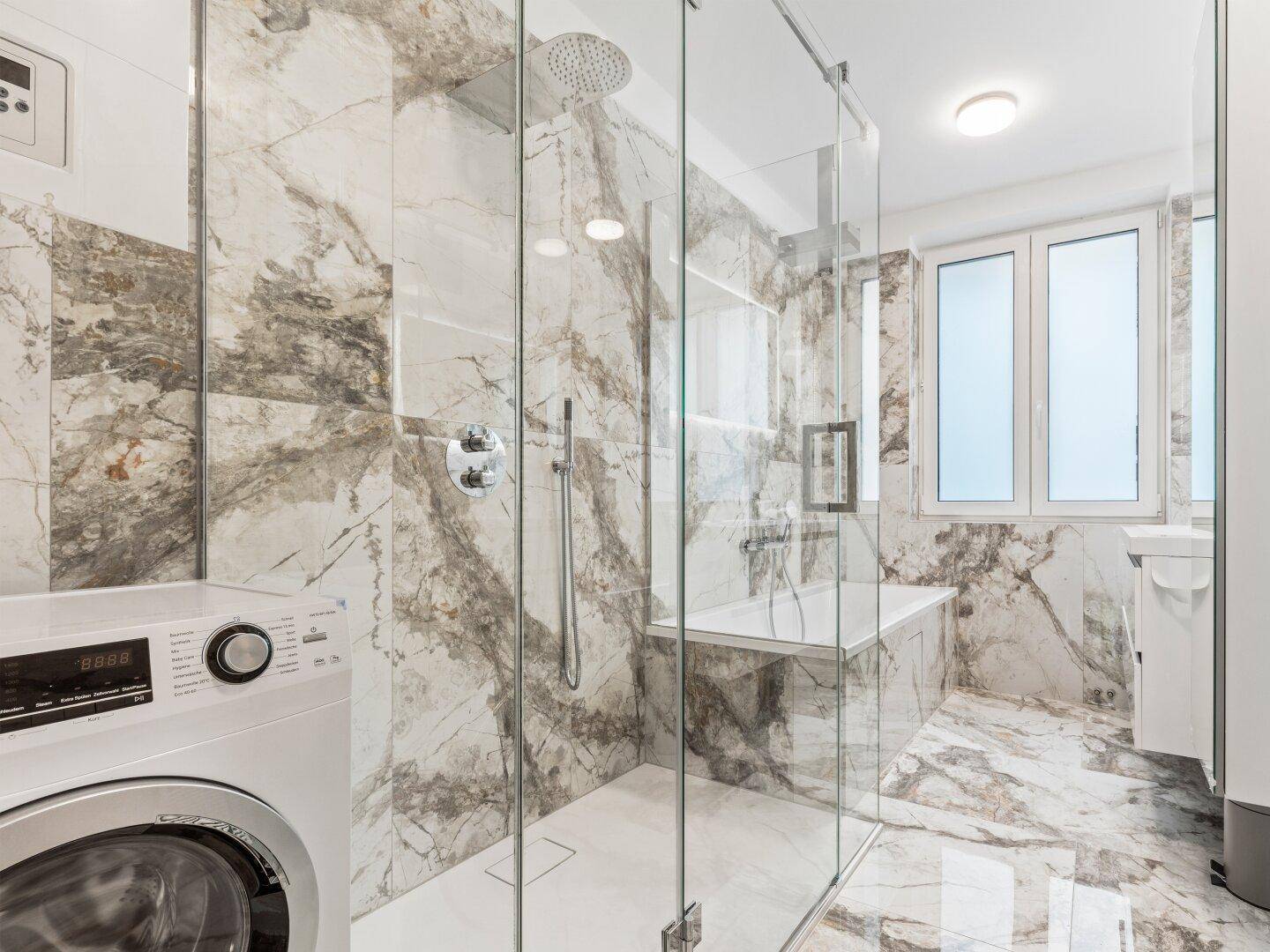 Modernes Badezimmer mit großer Glasdusche, Badewanne, Marmorfliesen und Waschmaschine.