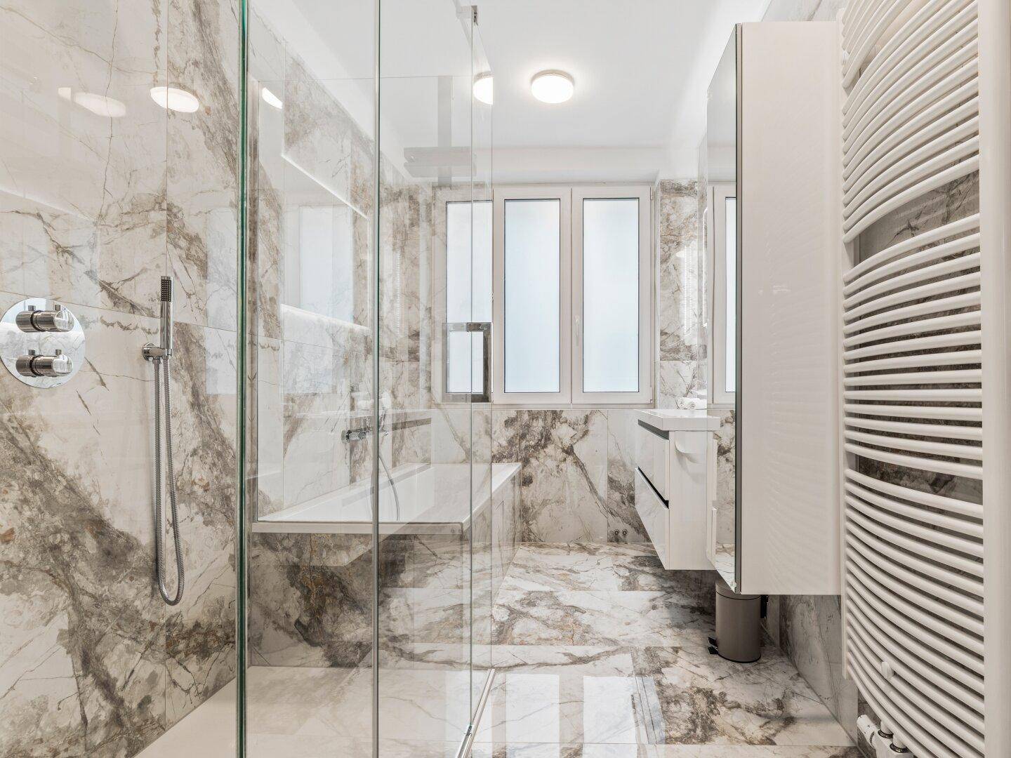 Elegantes Badezimmer mit Marmorfliesen, Glasdusche und beheiztem Handtuchhalter.