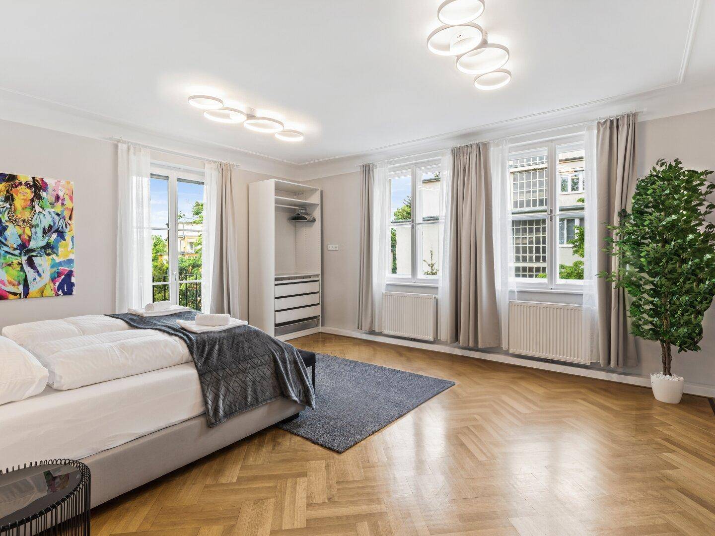 Helles Schlafzimmer mit Parkettboden, Einbauschrank und mehreren Fenstern.