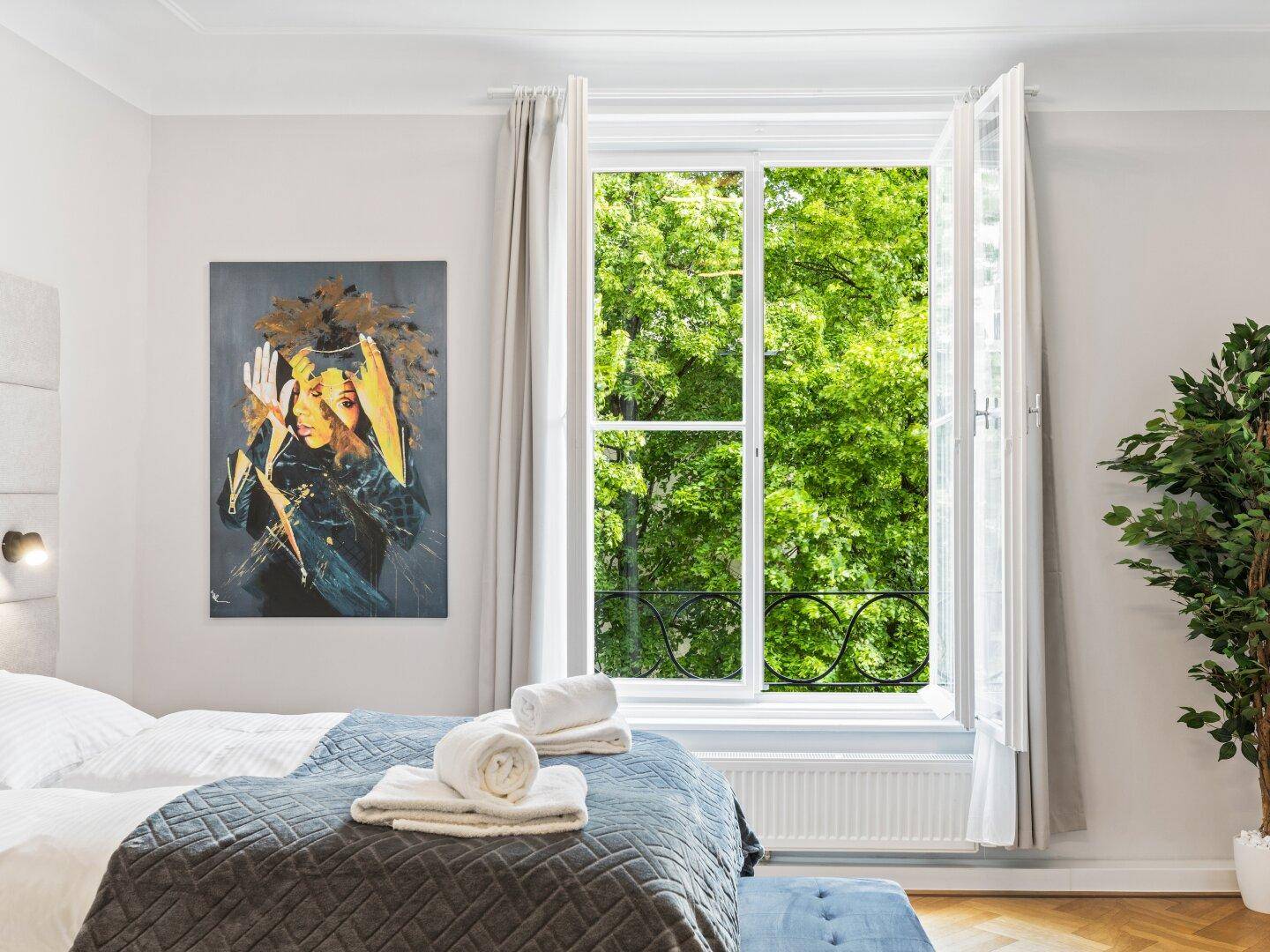 Helles Schlafzimmer mit Parkettboden, großem Fenster und Blick ins Grüne.