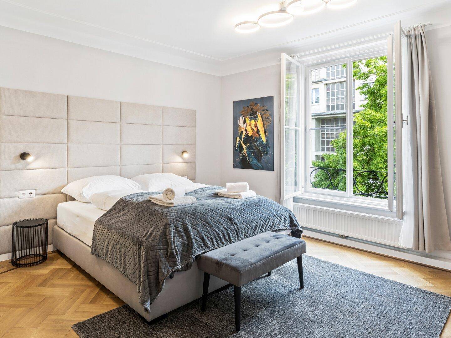 Komfortables Schlafzimmer mit gepolstertem Kopfteil, Parkett und Blick auf die Umgebung.