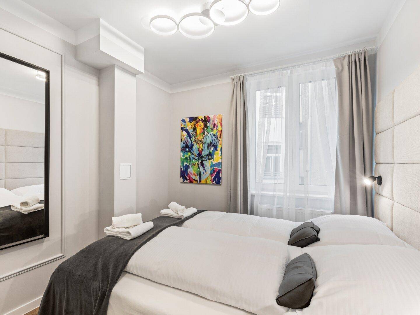 Modernes Schlafzimmer mit zwei Einzelbetten, Kunstwerk und großem Spiegel.