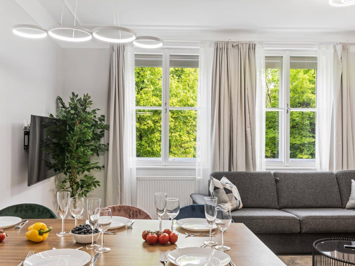 Lichtdurchfluteter Wohn- und Essbereich mit bequemer Couch und Blick auf grüne Bäume.