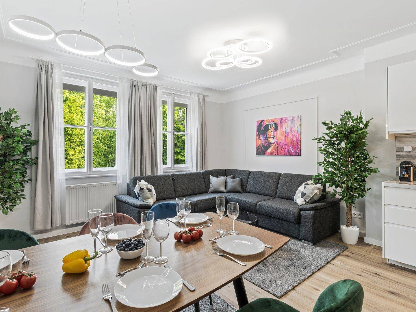 Geräumiger Wohn-Essbereich mit Kunstwerken, Ecksofa und Blick ins Grüne, verbunden mit der Küche.