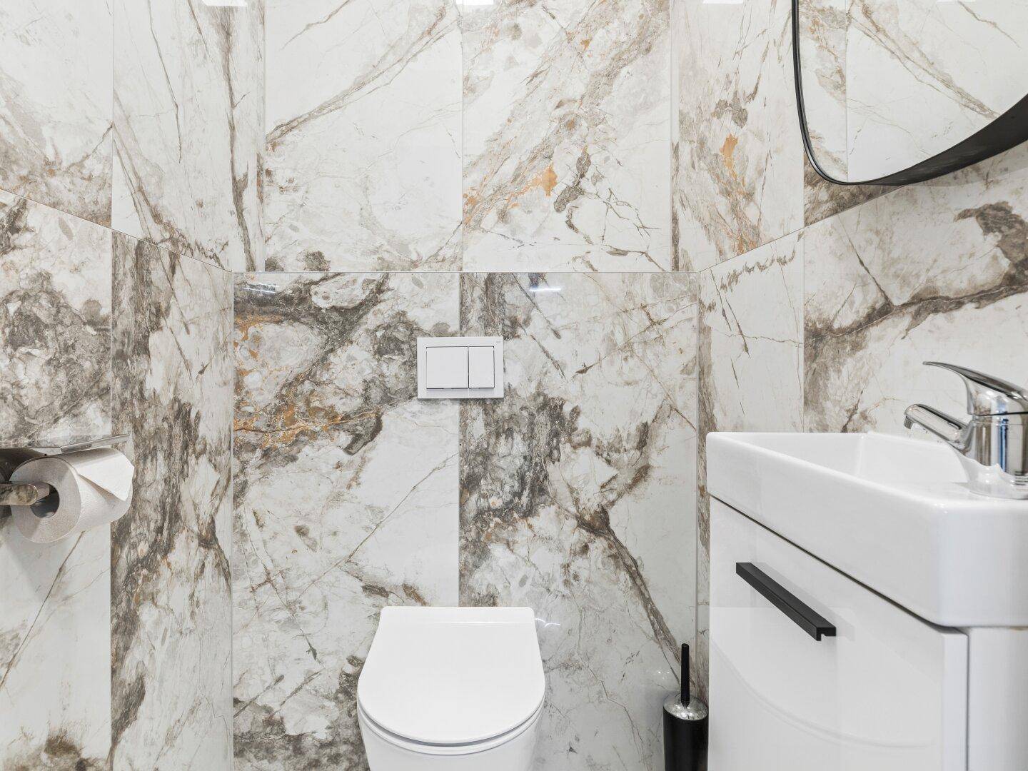 Modernes Gäste-WC mit Marmorfliesen, wandhängender Toilette und kleinem Waschbecken.