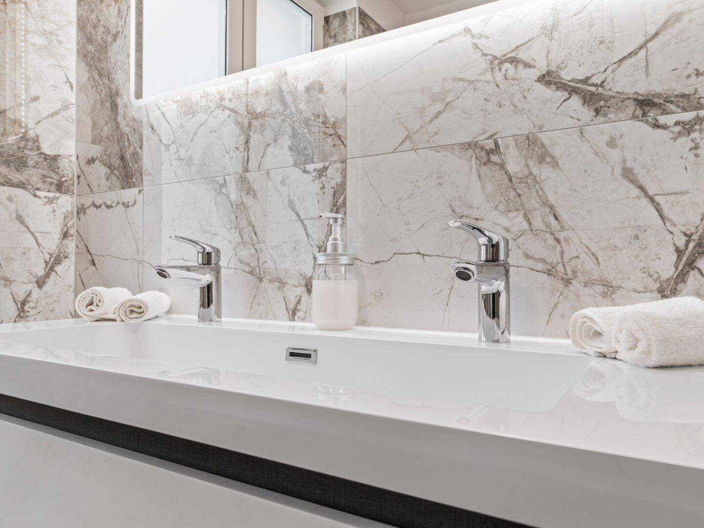 Doppelwaschbecken mit modernen Armaturen und Marmor-Rückwand im eleganten Badezimmer.