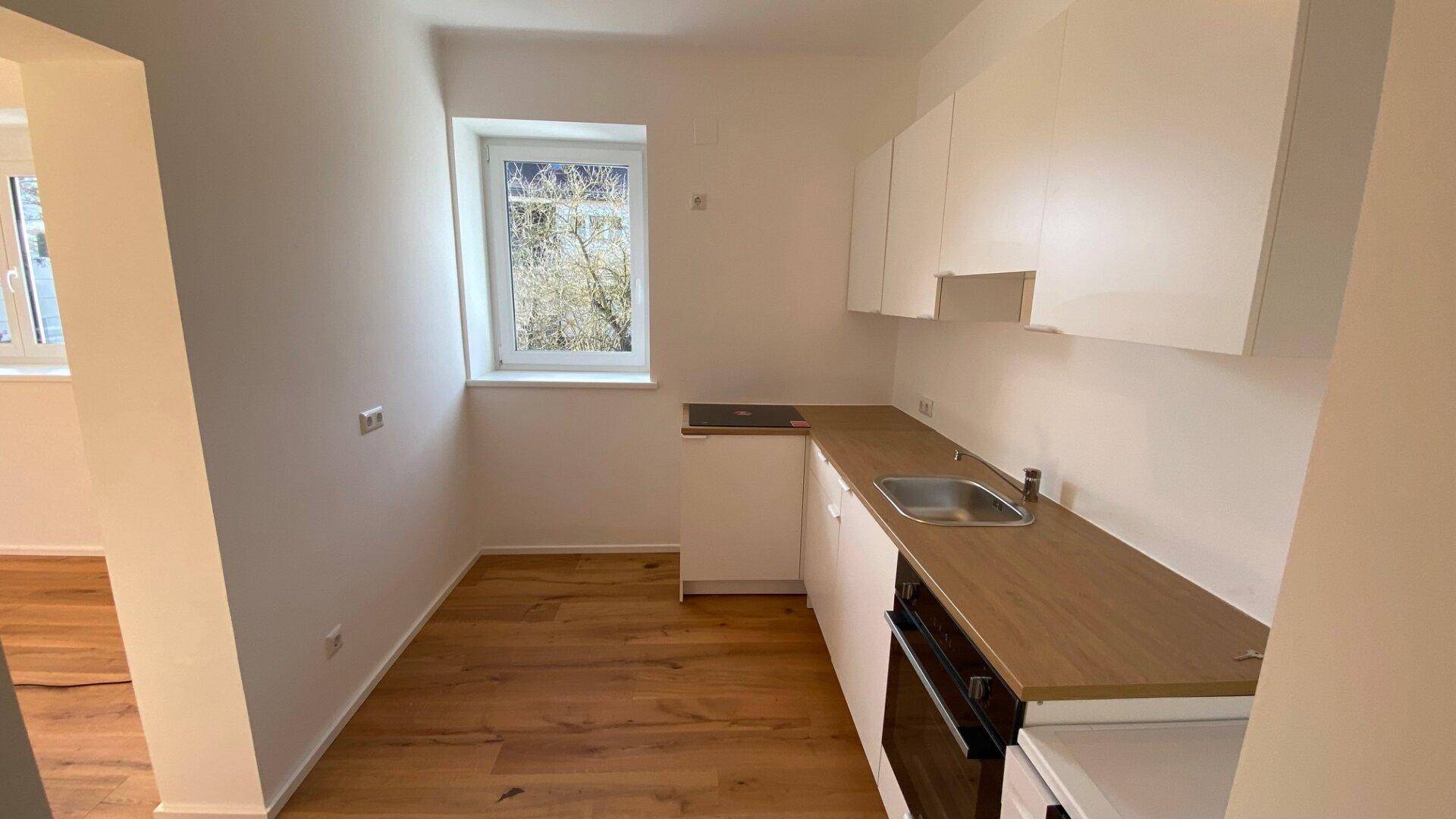 Moderne Einbauküche mit weißen Schränken, Holzarbeitsplatte und Fenster mit Blick ins Grüne.