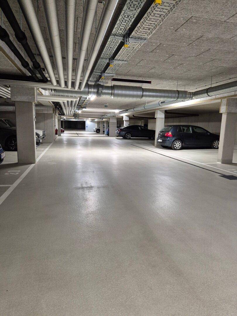 Geräumige Tiefgarage mit mehreren Stellplätzen und sichtbaren Installationen an der Decke.