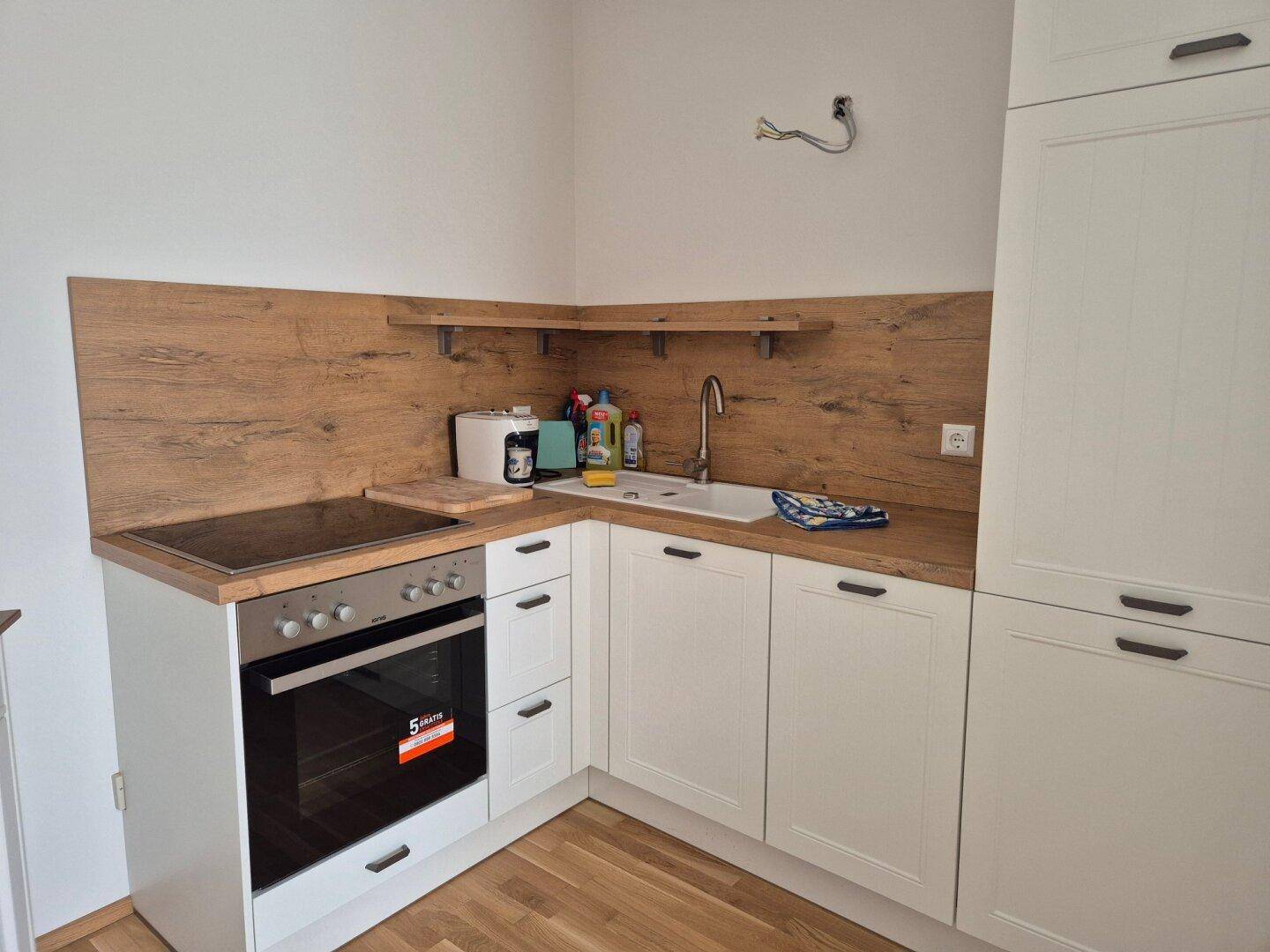 Funktionale Küche mit weißen Schränken, Holzoptik-Arbeitsplatte und integriertem Backofen.