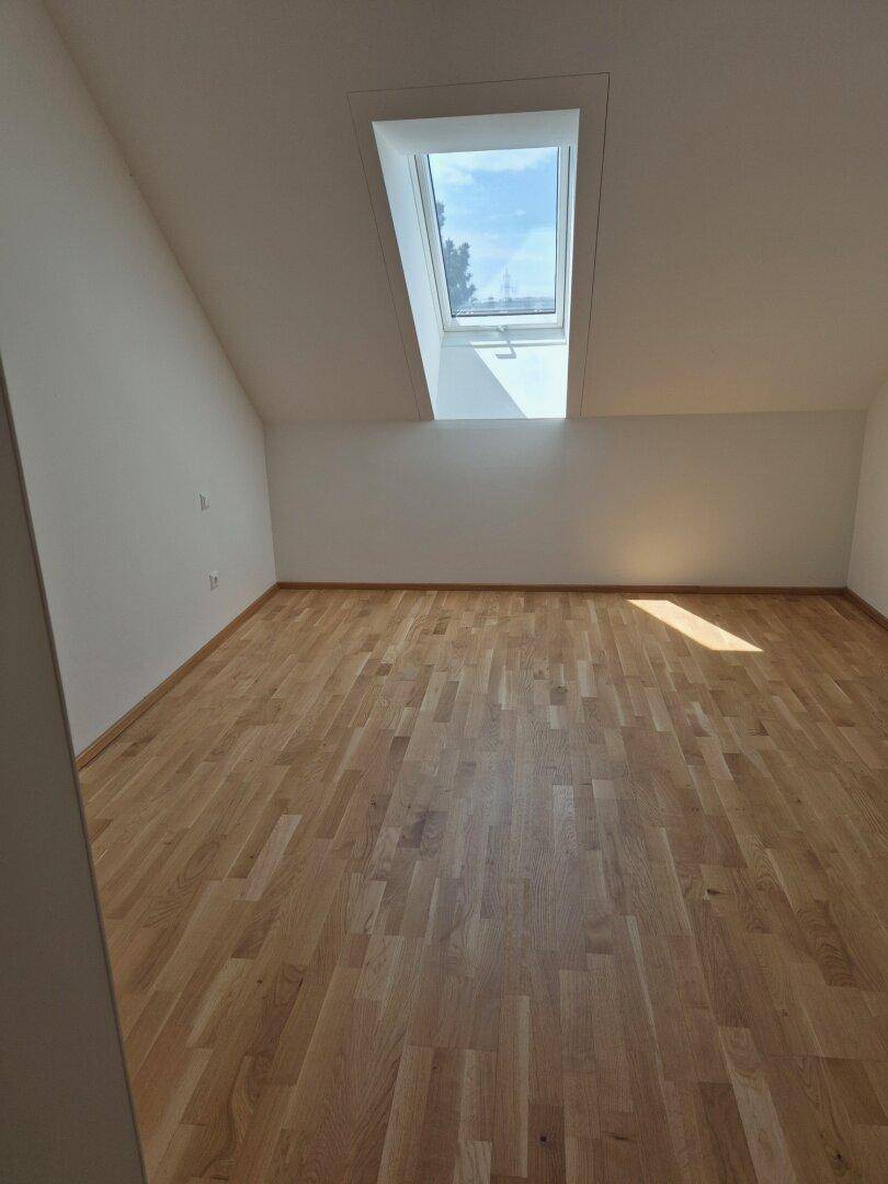 Heller Raum im Dachgeschoss mit Holzboden und einem großen Dachfenster.