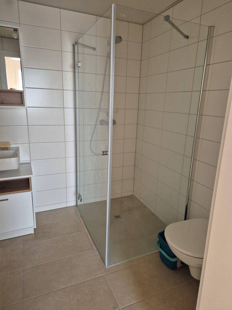 Modernes Badezimmer mit begehbarer Dusche, weißen Fliesen und einem einzelnen Waschbecken.