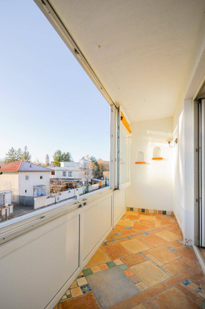 Heller Balkon mit Terrakotta-Fliesen und Ausblick auf die umliegenden Häuser und Bäume.