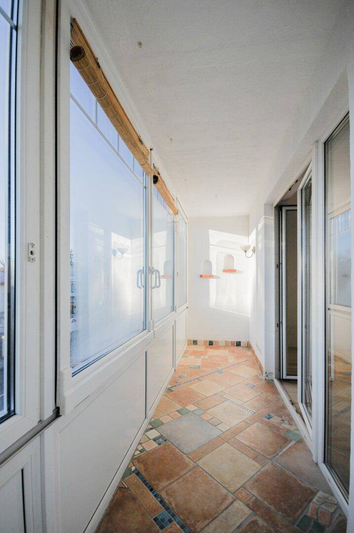 Langer, verglaster Balkon mit Terrakotta-Fliesen und Ausblick auf die Umgebung.