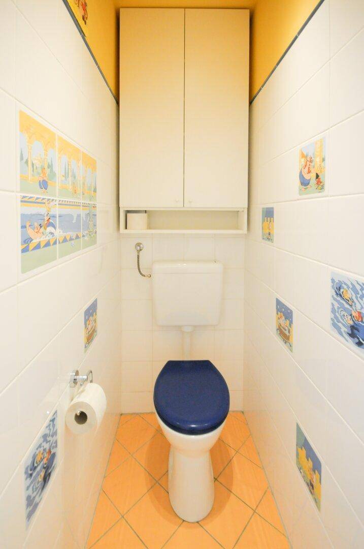 Separate Toilette mit WC und Wandfliesen, die mit verspielten Motiven verziert sind.
