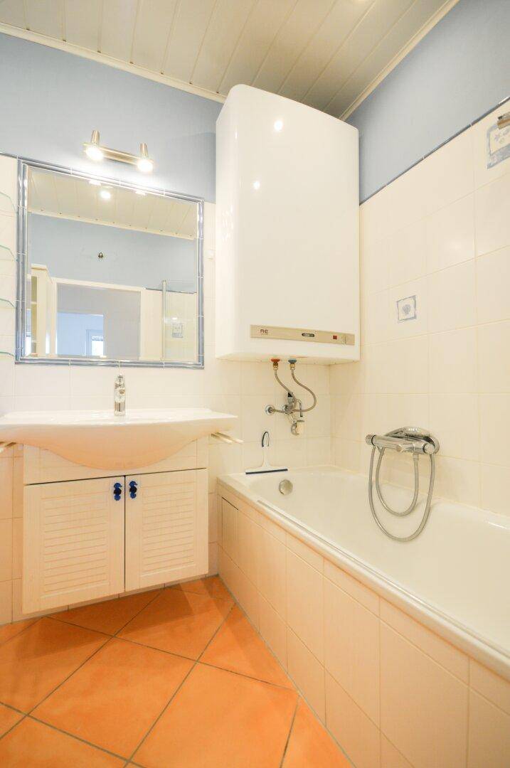 Badezimmer mit Badewanne, Waschbecken und Boiler, ausgestattet mit Terrakotta-Fliesen.